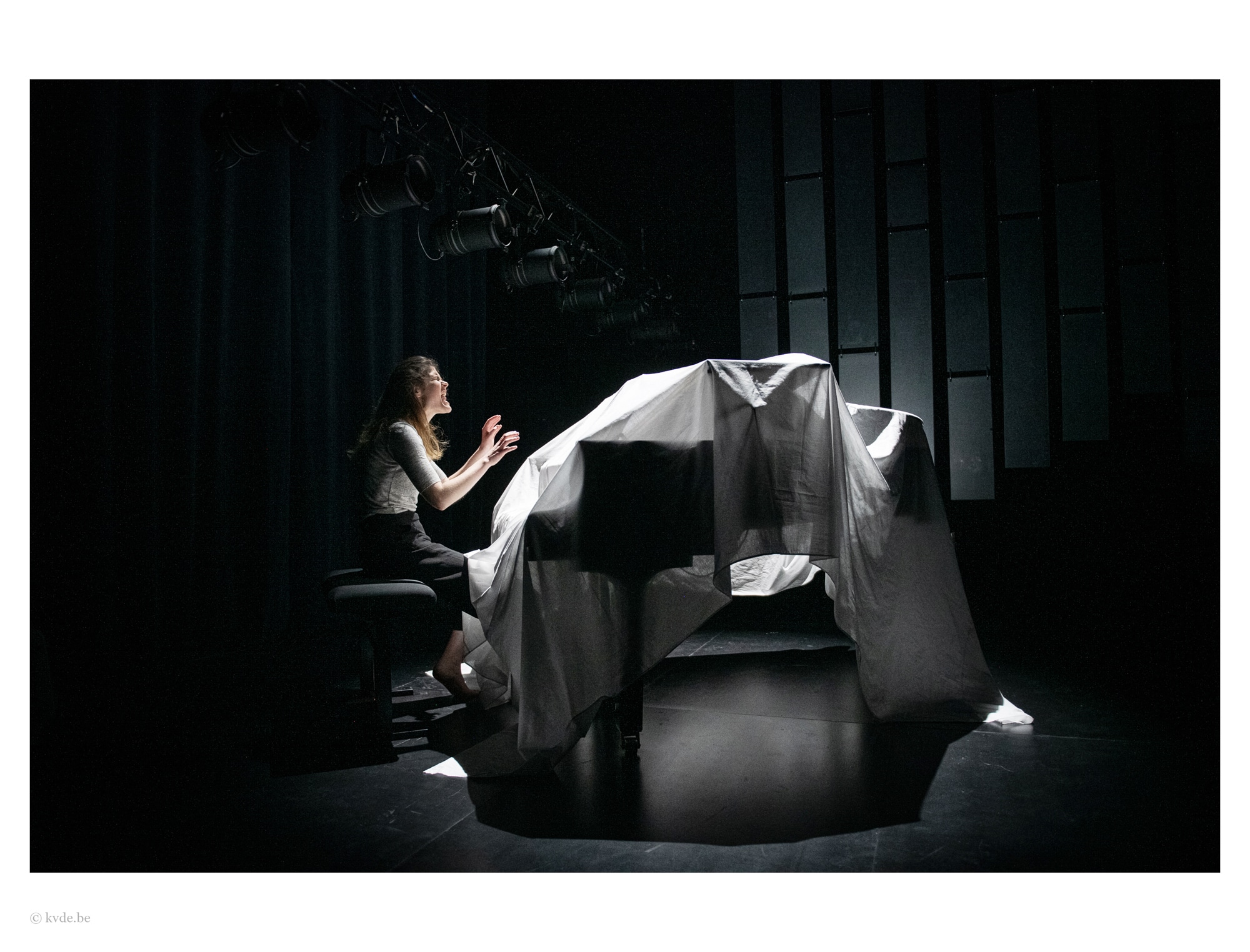 une femme qui chante et joue du piano qui est recouvert par un drap blanc